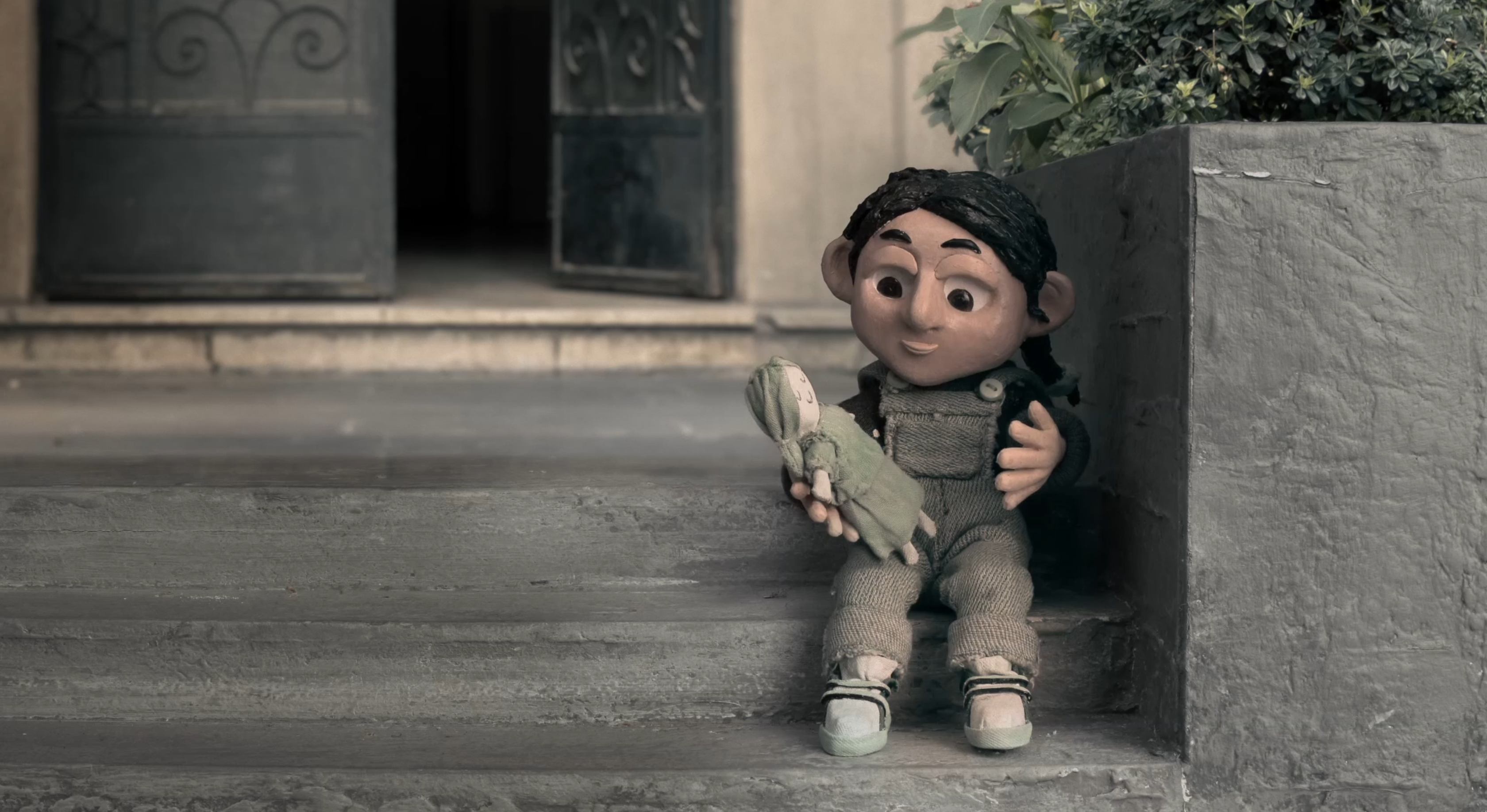 A little girl holding her doll perched outside Vladimir's house